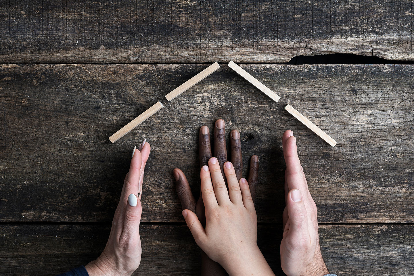 Hände formen Haus aus Holzstäben.