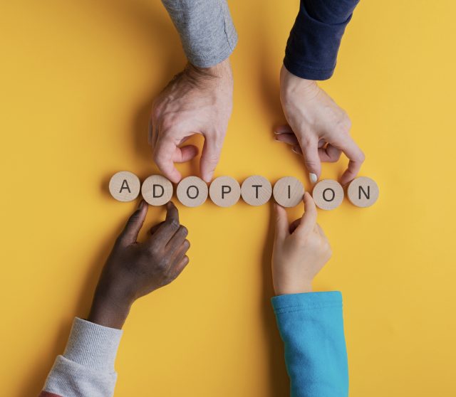 Vier Hände, Wort "Adoption" auf Holzscheiben.
